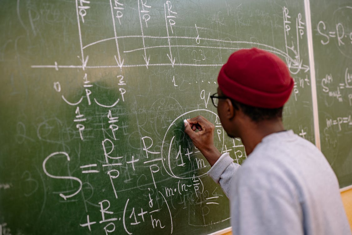 Free Student writing complex mathematical equations on a chalkboard in a classroom setting. Stock Photo