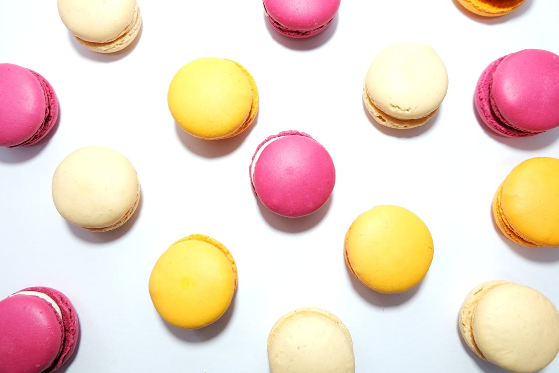 Free Vibrant pink, yellow, and cream macarons arranged in a flatlay on a white background. Stock Photo