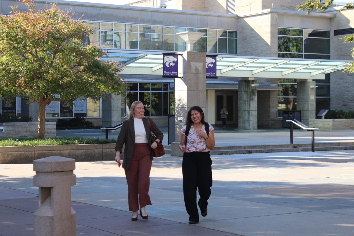 Two women walk and laugh together across Bosco Plaza outside of the K-State Student Union.