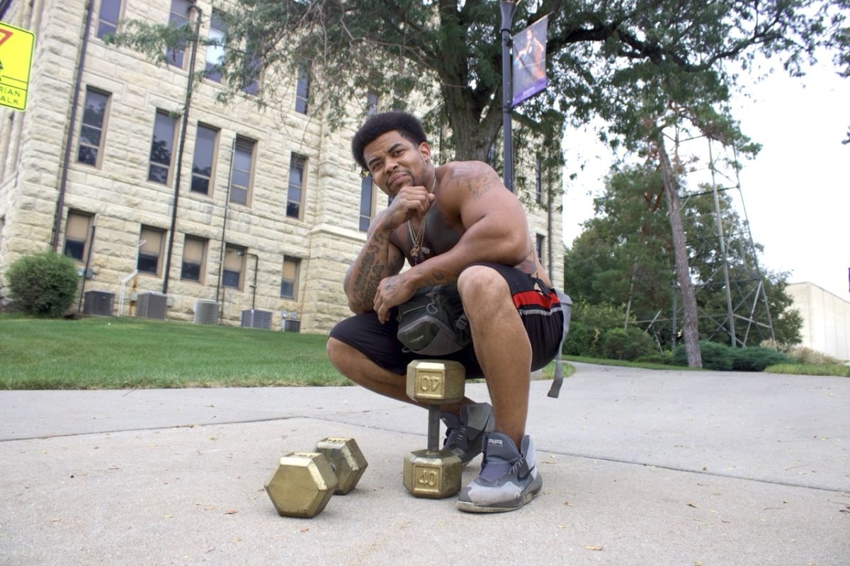 Bryan Vereen crouches and poses with his iconic dumbbells on K-State's campus. Vereen is known for walking around Manhattan and curling gold dumbbells down Anderson Avenue.
