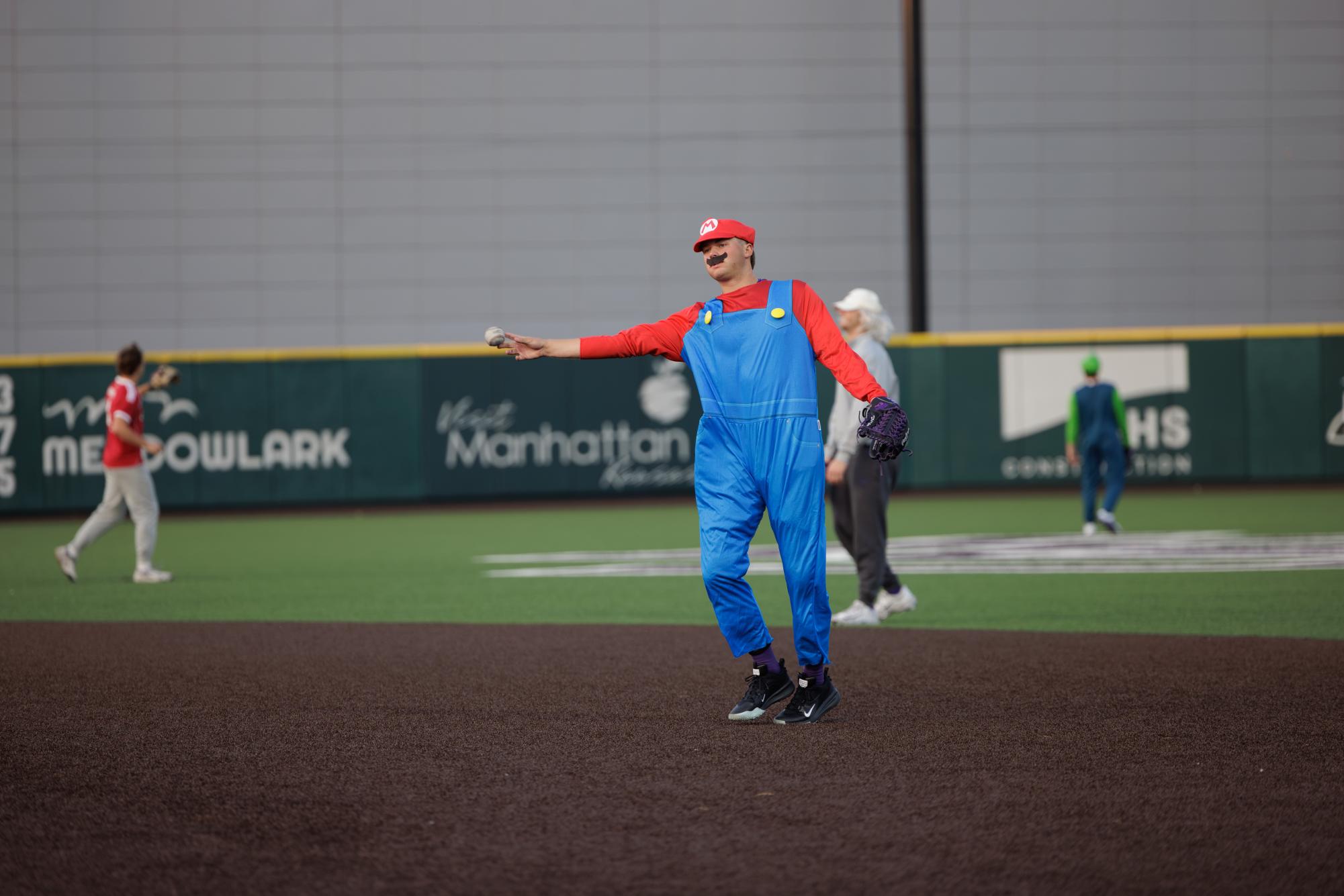Dressed as the video game character Mario, K-State's Jackson Hulcher throws a baseball to first base during the Wildcats' ALS Halloween baseball game on October 29.